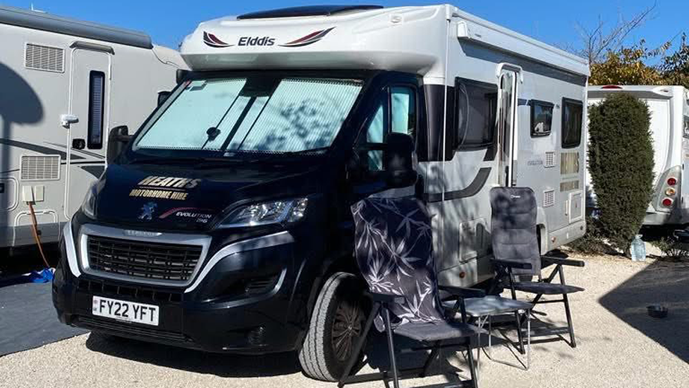 Elddis motorhome with the awning open and outdoor camping chairs set up at a campsite