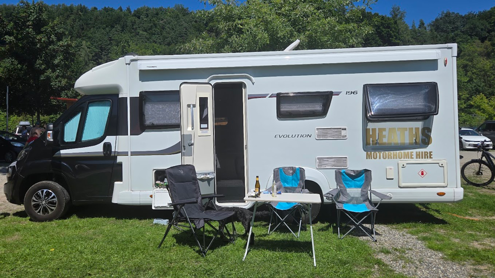 Heaths Motorhome Hire motorhome set up at a campsite with outdoor chairs and awning on a sunny day