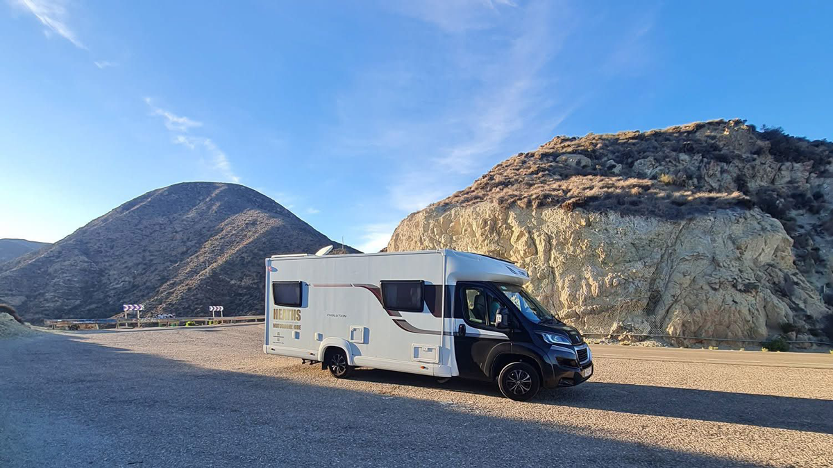 Motorhome parked at a scenic mountain layby with rocky cliffs and blue sky in the background