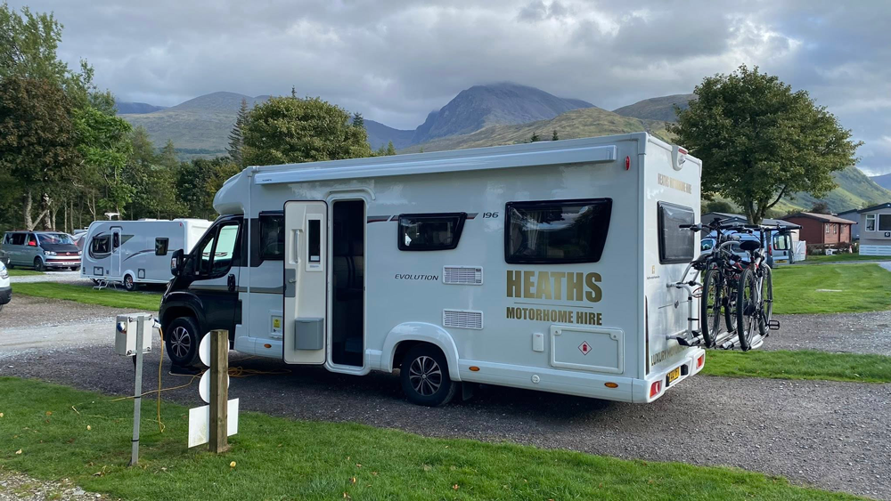 Heaths Motorhome Hire motorhome parked at a lakeside campsite with mountains in the background and bikes on the rear rack