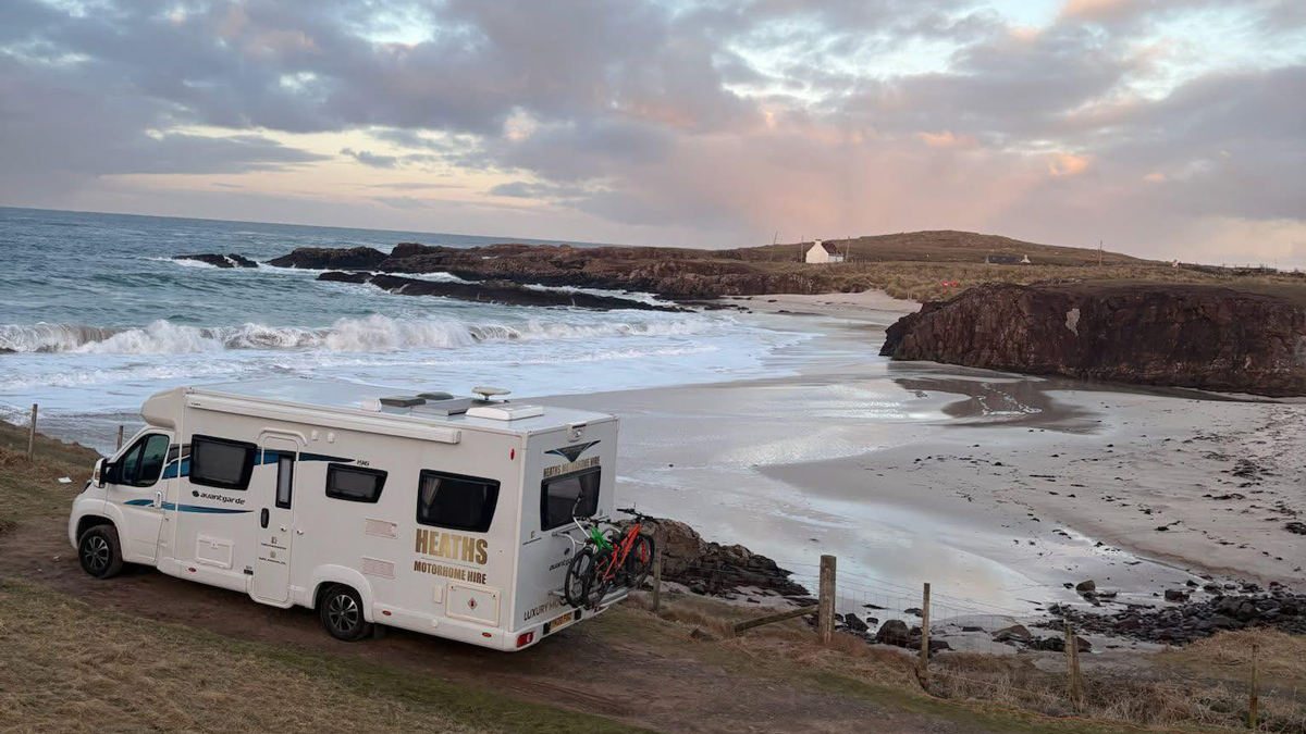 Heaths Motorhome Hire motorhome parked overlooking a rugged coastal beach at sunset with bikes on the rear rack