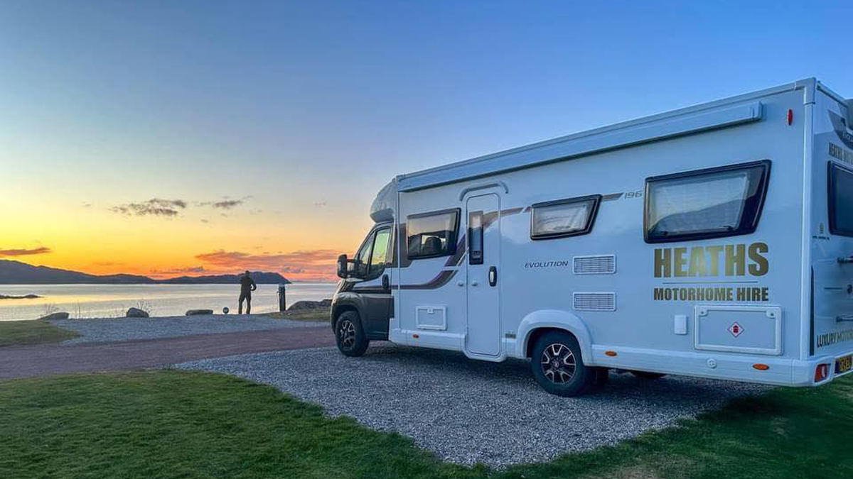 Heaths Motorhome Hire motorhome pitched on a gravel campsite by the sea at sunset